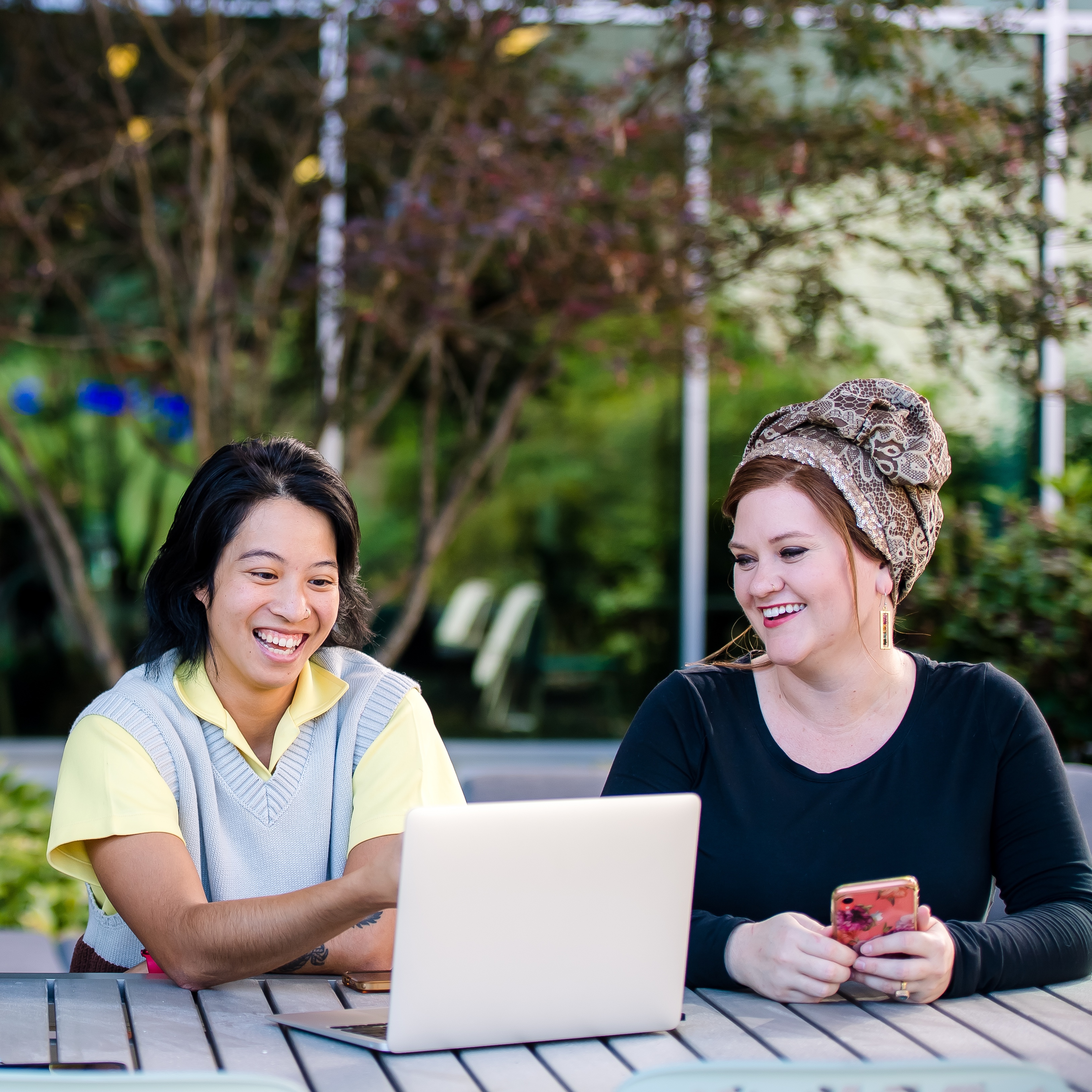 Two Capital One ADP associates sit outside and look on a laptop together