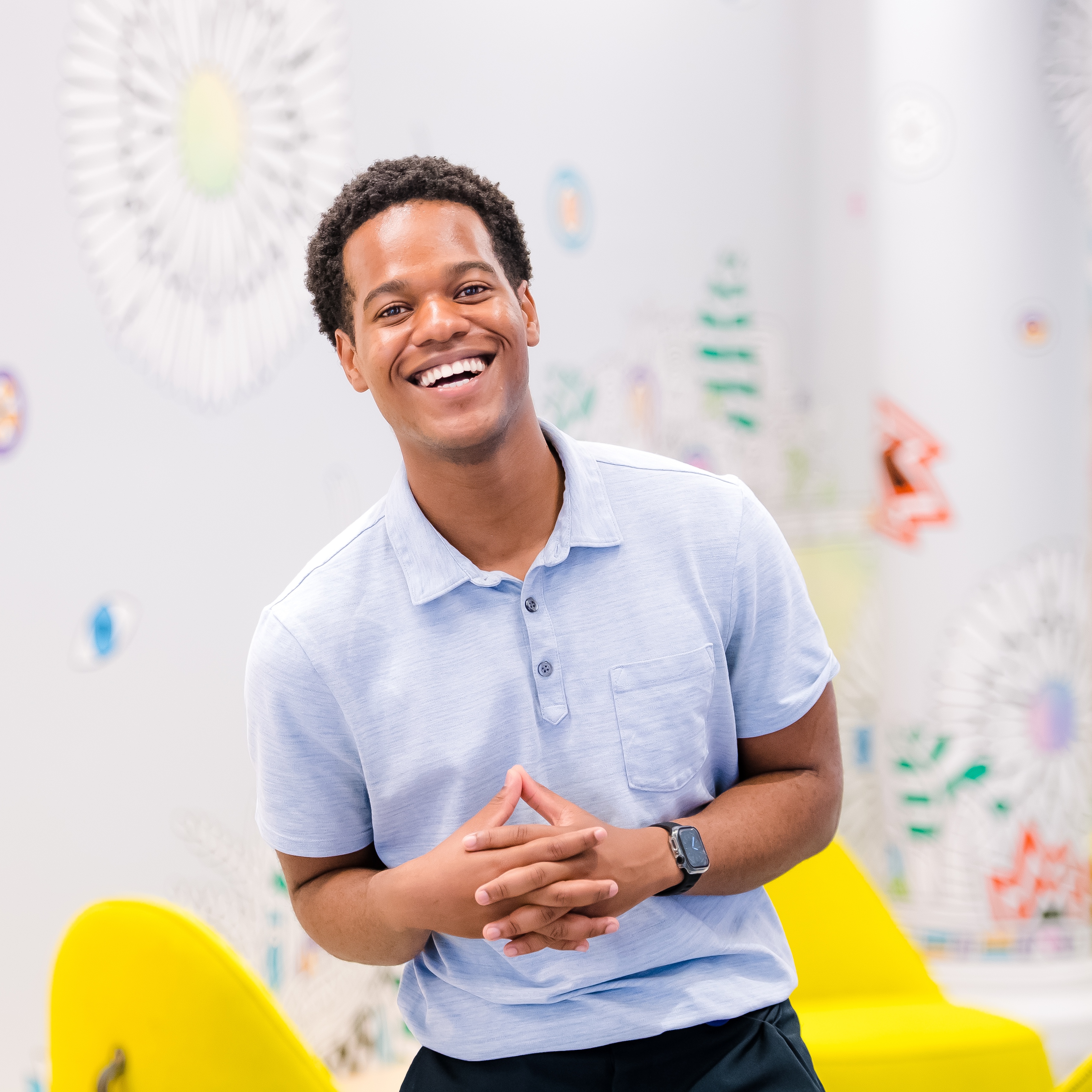 Capital One ADP associate stands in front of a white wall with colorful designs with his hands folded