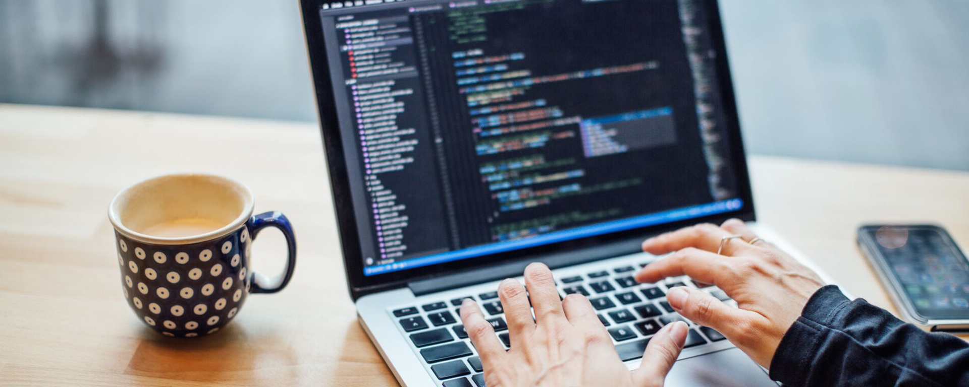 A close up of a Capital One associate working on their laptop with coding on the screen next to a mug