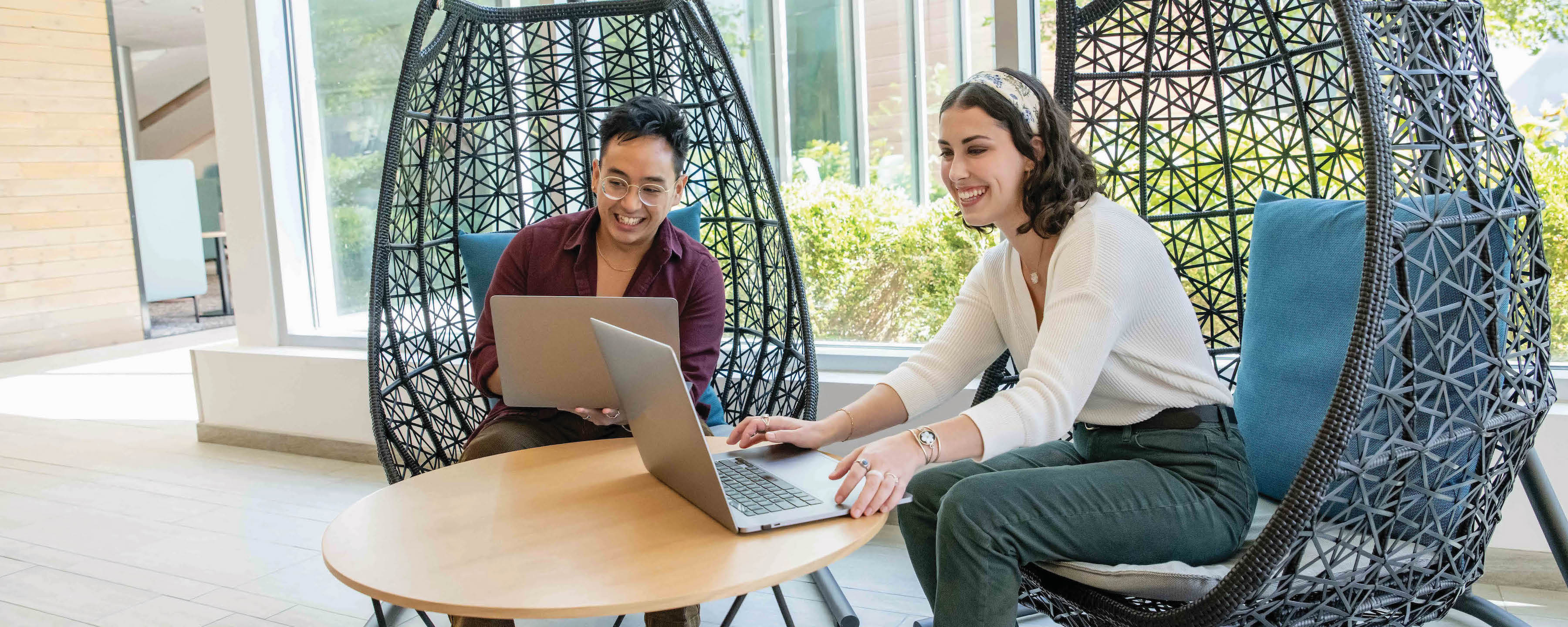 Two Capital One associates sit in swing chairs working on their laptops