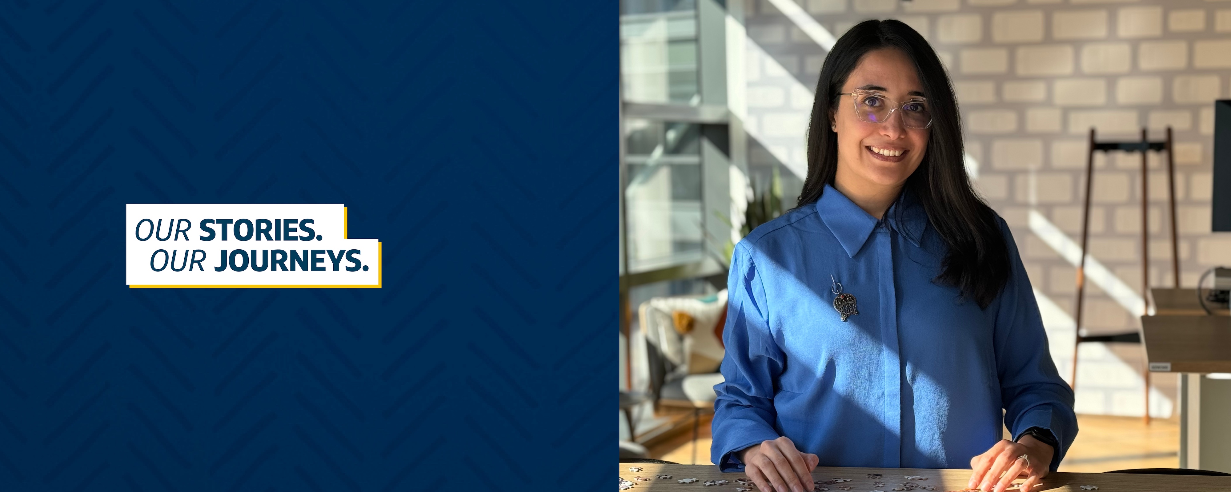 Capital One associate Fatma stands at a wooden table wearing glasses and a blue shirt, the title "Our Stories, Our Journeys" next to the picture