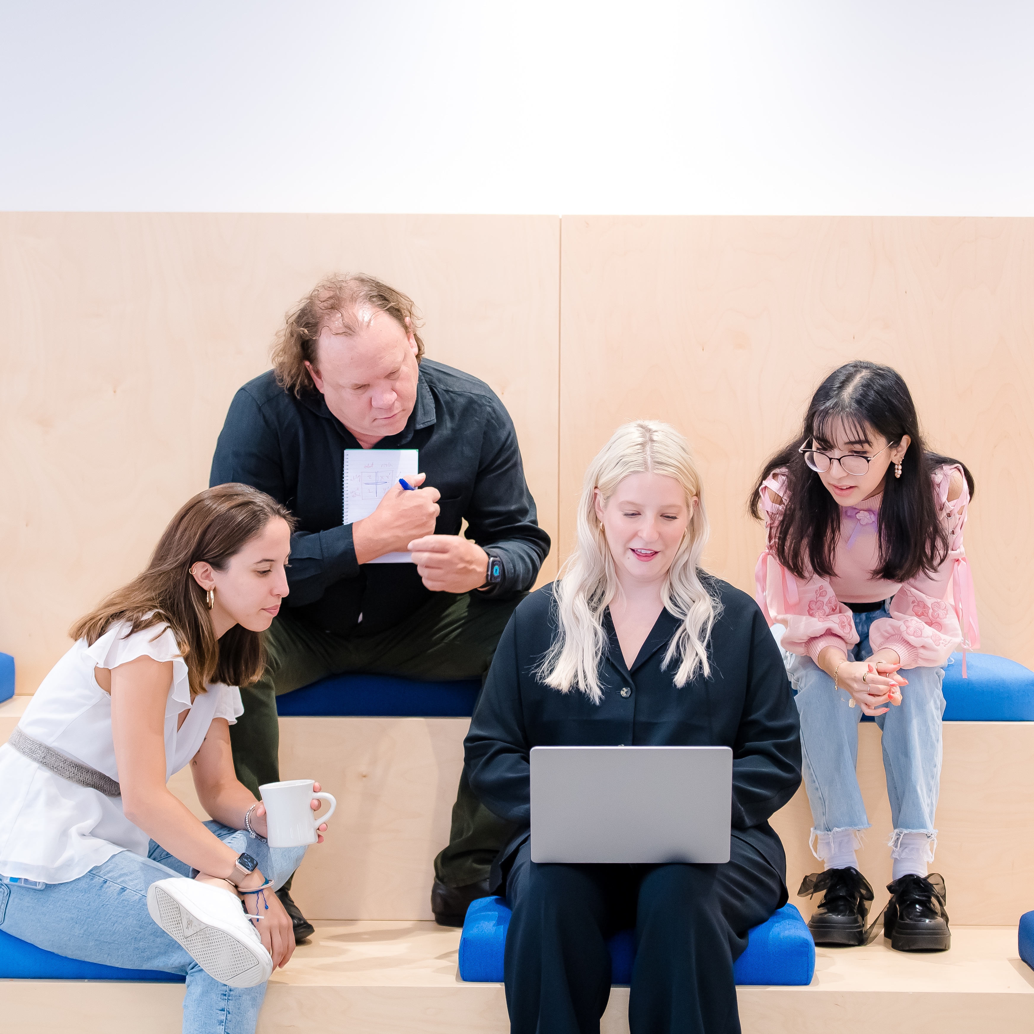 A group of 4 Capital One PDP associates sit on a wooden step bench and look on a laptop together
