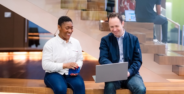Two Capital One Strategy associates sit on a bench and look at a laptop talking