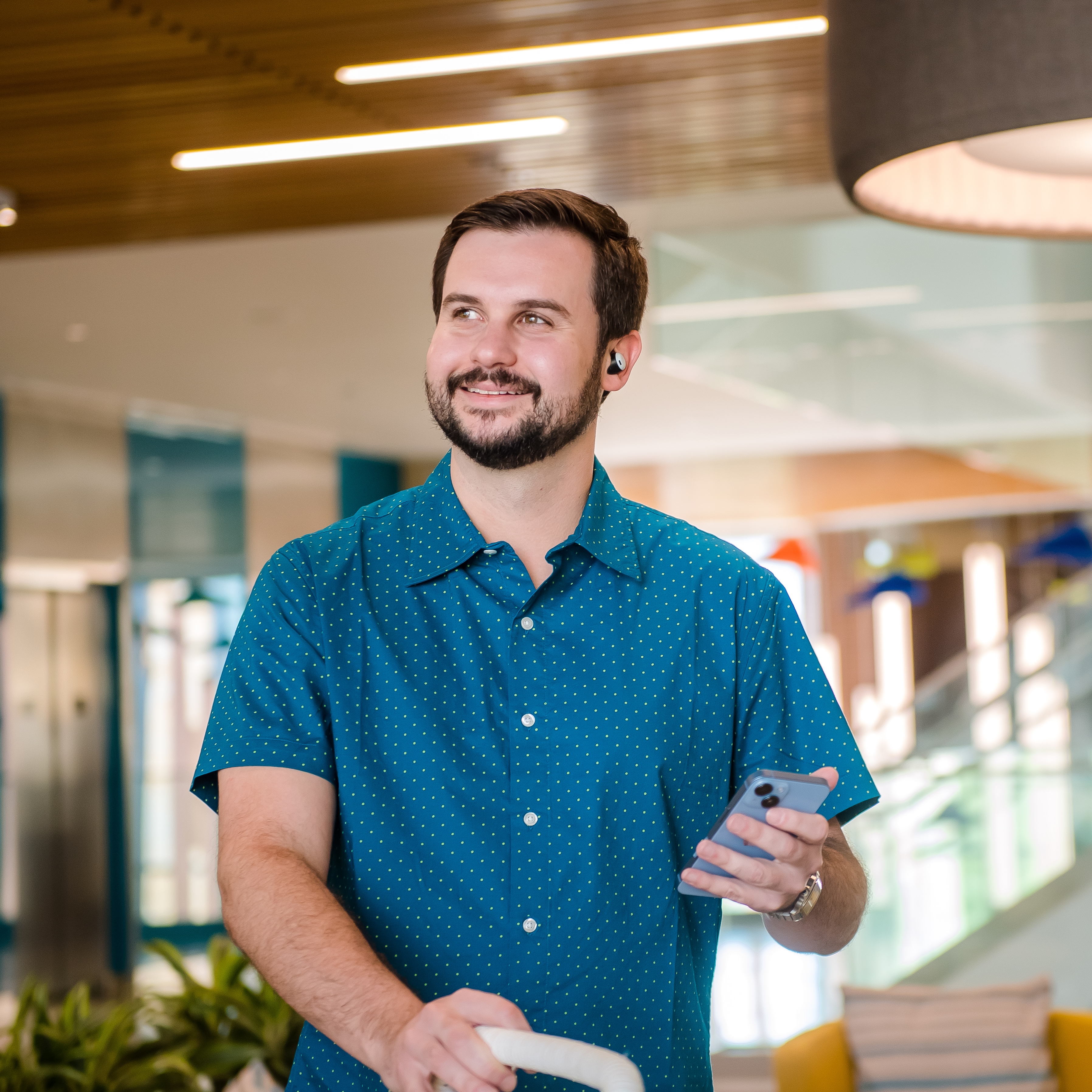 Capital One associate stands holding his phone wearing a blue shirt