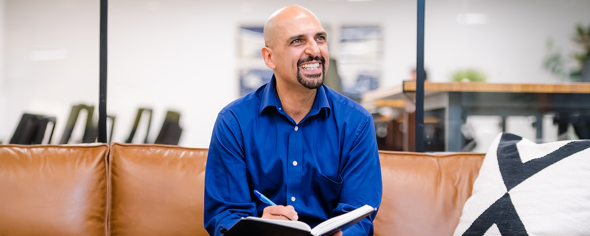 Capital One associate sits on a leather couch writing in a notebook and smiles