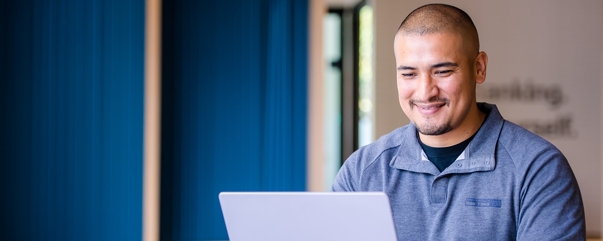 A Capital One associate smiles wearing a blue sweater working on a computer in the Capital One offices
