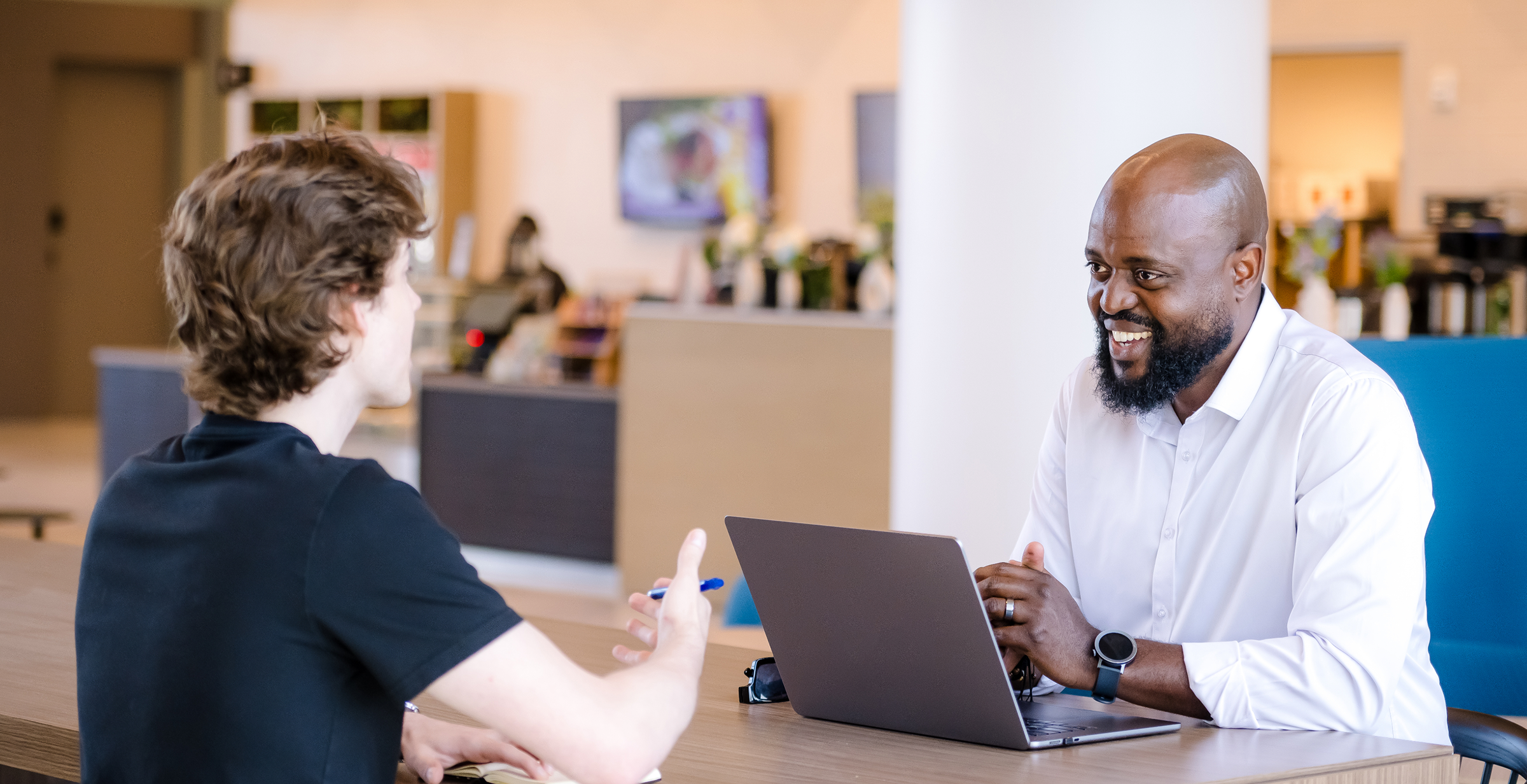 Two Capital One associates sit at a table talking, one with his laptop