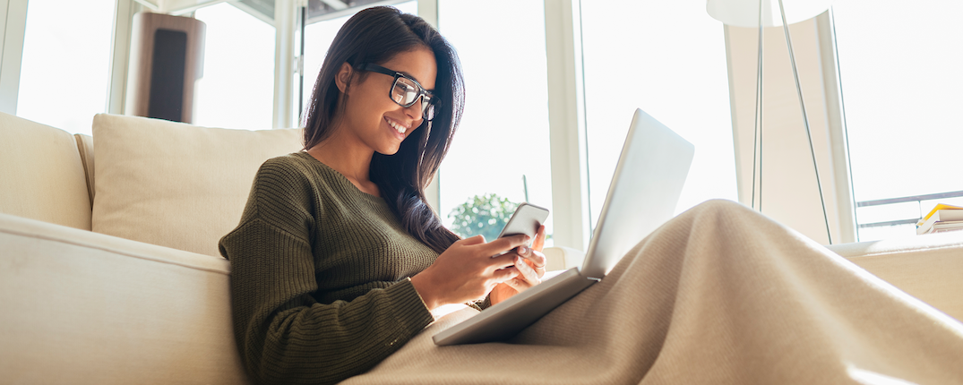 Capital One first generation associate sits on a couch with a blanket working on her laptop