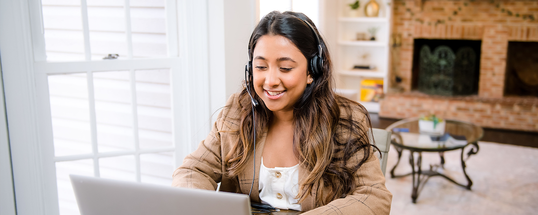Capital One associate sits at her kitchen table working on her laptop and talking with a headset on