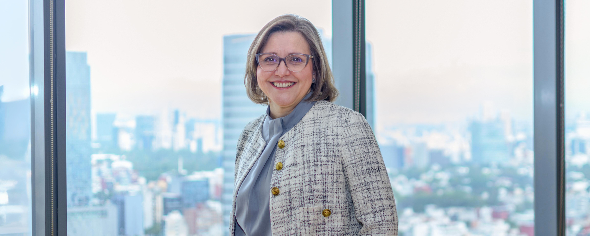 Capital One Mexico leader Judith stands and smiles in front of a window overlooking a city