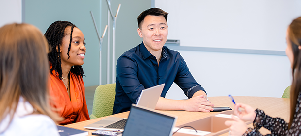 Capital One Strategy Consulting associates sit around a table and talk with their laptops out