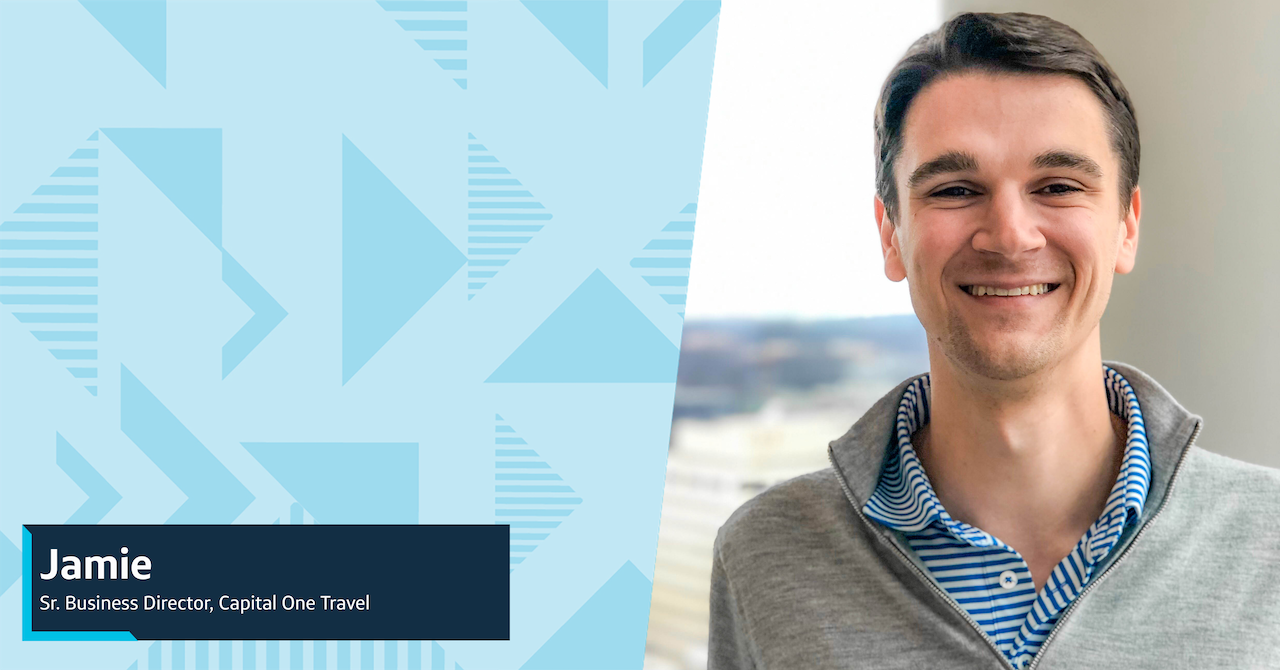 Jamie, Capital One Director, smiles wearing a gray sweater and blue striped shirt in front of a gray wall